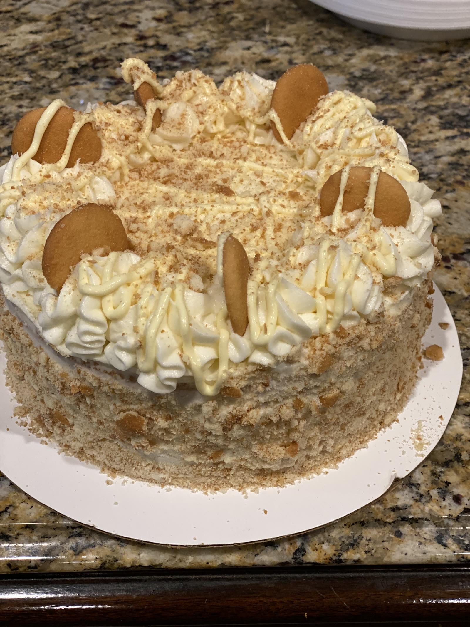 Banana pudding layer cake topped with vanilla wafers, whipped cream swirls, and cookie crumble