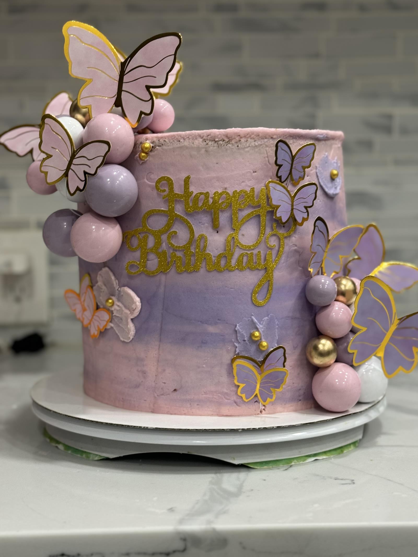 Lavender and pink watercolor birthday cake covered in gold-trimmed butterflies and shimmer pearls
