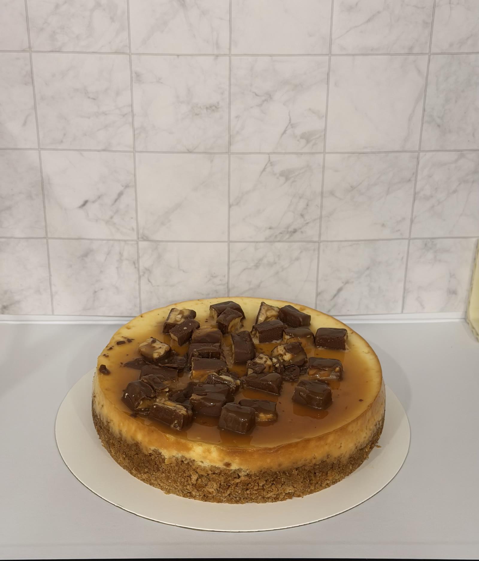 New York cheesecake topped with chopped chocolate candy bars and caramel drizzle