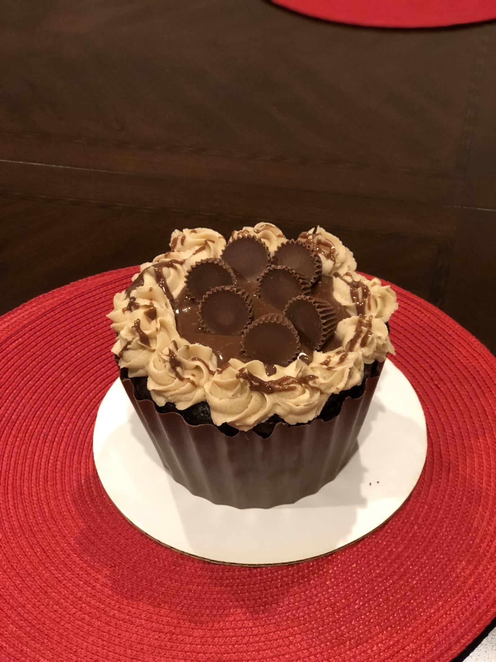 Giant peanut butter cup cake in a chocolate shell topped with peanut butter cups and piped frosting