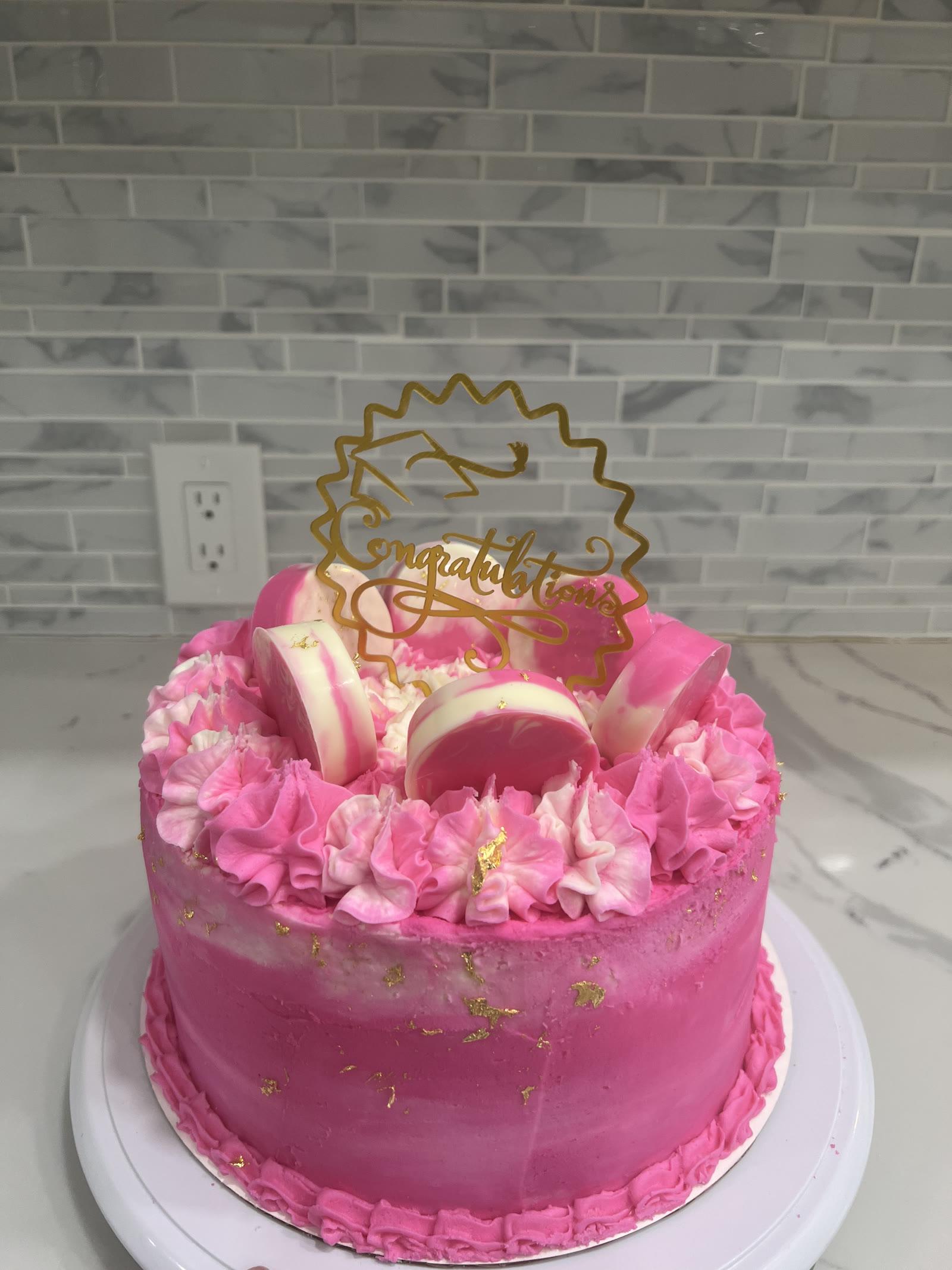 Hot pink graduation cake with gold Congratulations topper, ruffle piping, and gold leaf accents