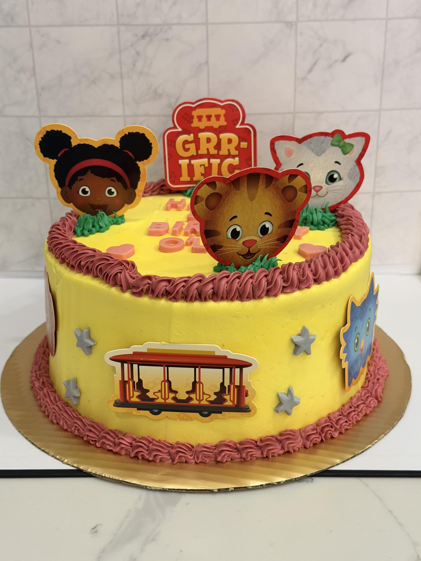 Yellow children's character birthday cake with dusty rose piping, cartoon toppers, and a trolley decal