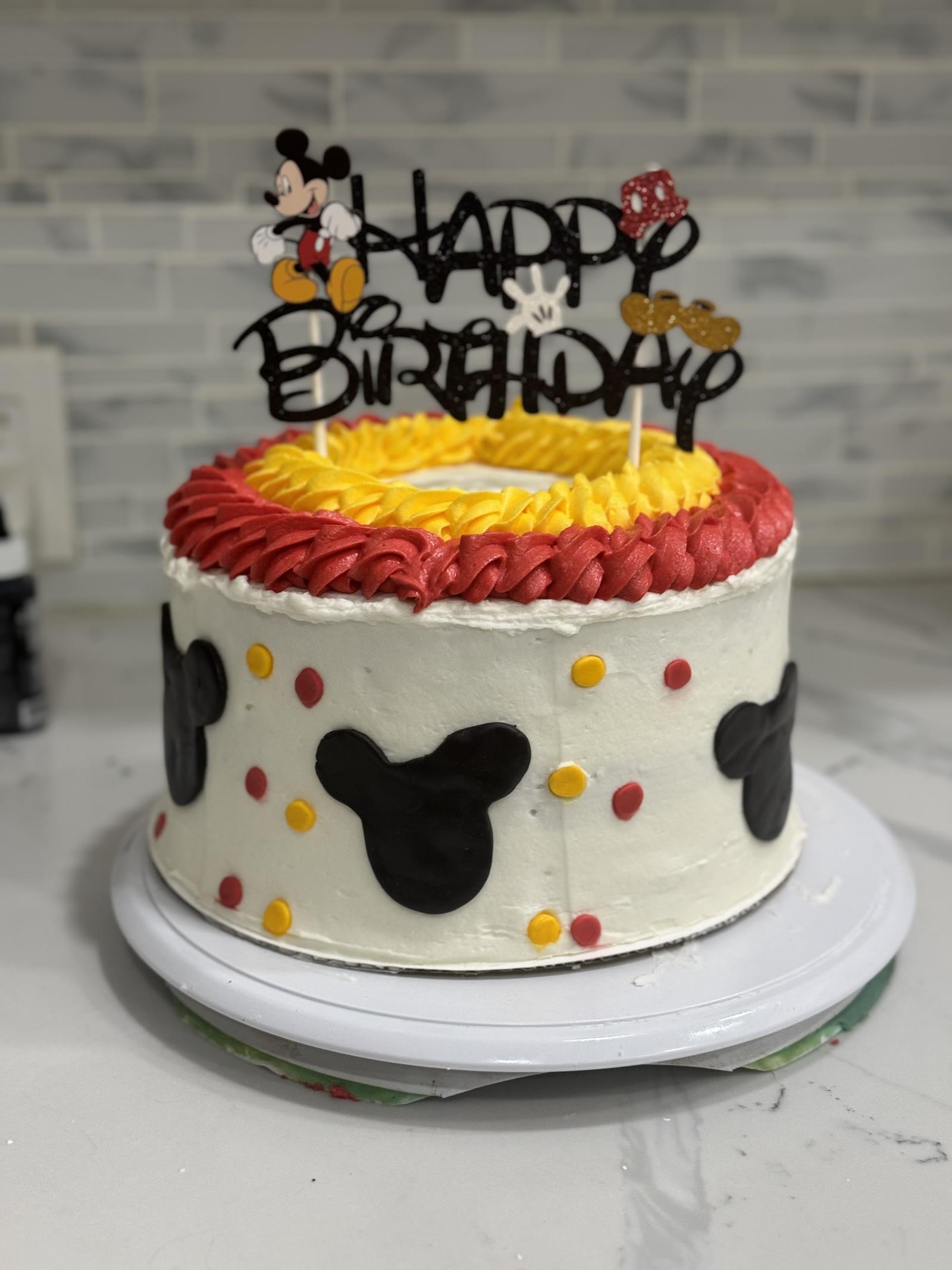 Mickey Mouse birthday cake with red and yellow piping, chocolate Mickey silhouettes, and a Happy Birthday topper