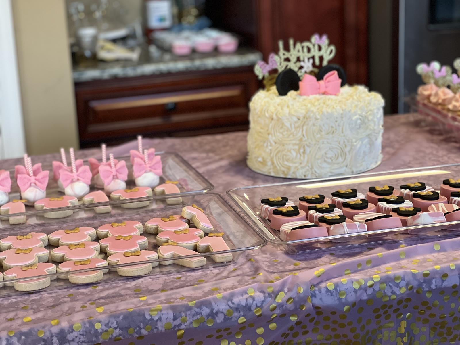 Pink and gold themed dessert table with rosette cake, decorated cookies, cake pops, and chocolate-covered Oreos