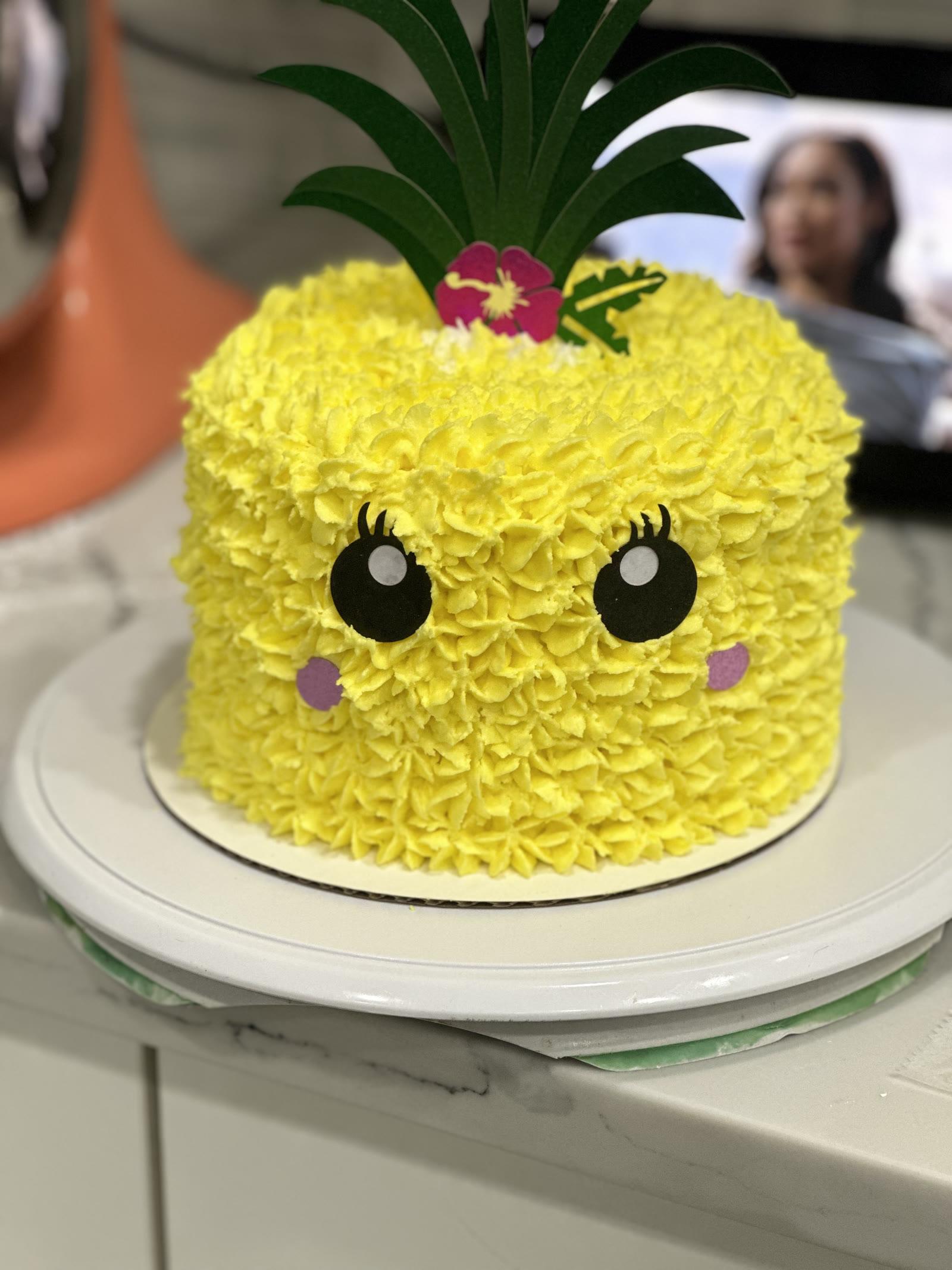 Yellow pineapple character cake with piped texture, a cute face, and a leafy top